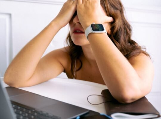 Woman showing stress or tiredness with hands on face at a desk with a laptop.